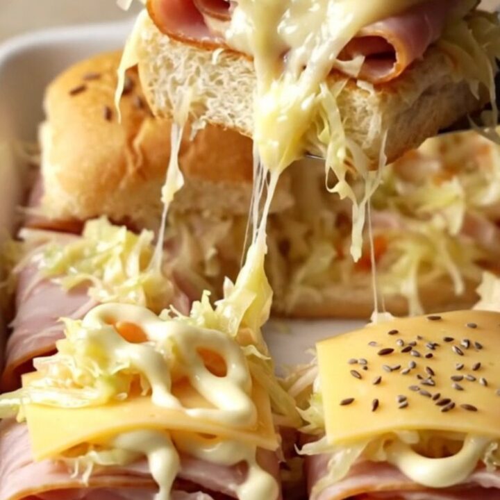 A golden-brown tray of turkey Reuben sliders with melted Swiss cheese and caraway seeds.