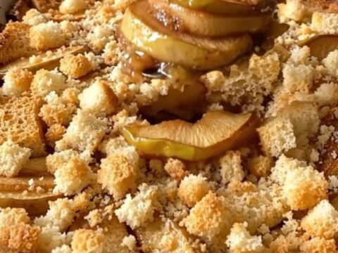 A golden-brown apple brown betty in a white ceramic dish, showing bubbling cinnamon syrup and crispy bread cubes.
