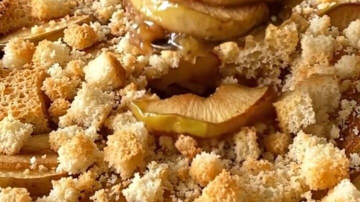 A golden-brown apple brown betty in a white ceramic dish, showing bubbling cinnamon syrup and crispy bread cubes.
