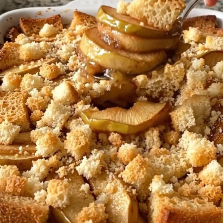 A golden-brown apple brown betty in a white ceramic dish, showing bubbling cinnamon syrup and crispy bread cubes.