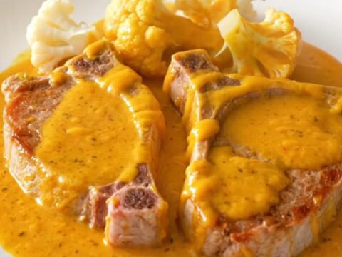 A close-up view of cooked pork chops and cauliflower florets coated in a creamy orange cheddar sauce in a slow cooker.