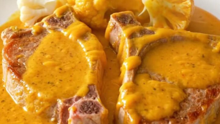 A close-up view of cooked pork chops and cauliflower florets coated in a creamy orange cheddar sauce in a slow cooker.