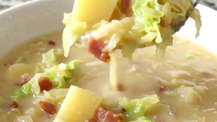 A close-up of creamy Colcannon soup in a white bowl, showing gold potato cubes, cabbage, and bacon.