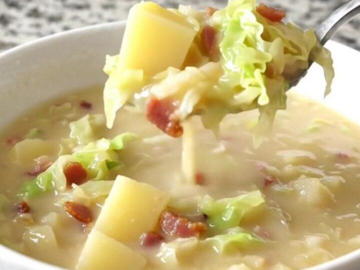 A close-up of creamy Colcannon soup in a white bowl, showing gold potato cubes, cabbage, and bacon.