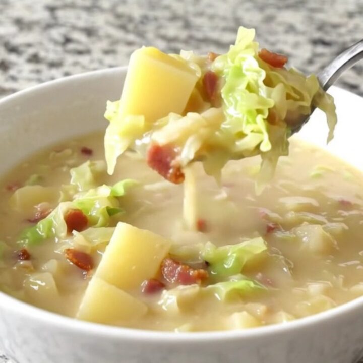A close-up of creamy Colcannon soup in a white bowl, showing gold potato cubes, cabbage, and bacon.