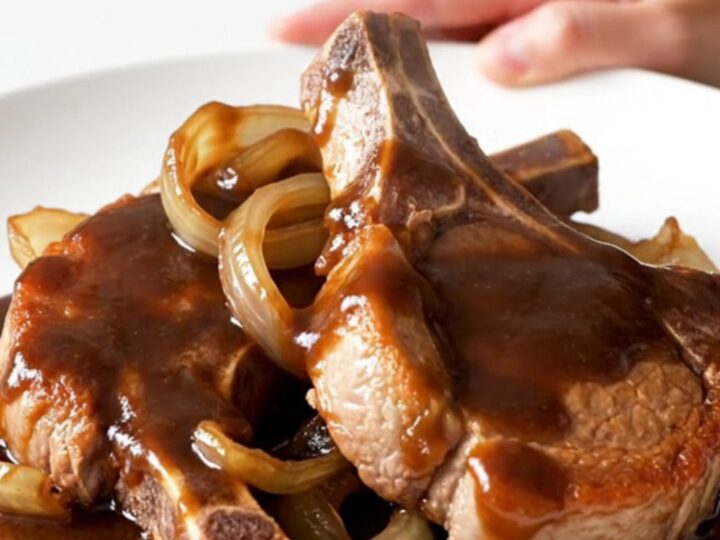 A close-up of tender, bone-in pork chops glazed in a dark, glossy root beer barbecue sauce with soft onions.
