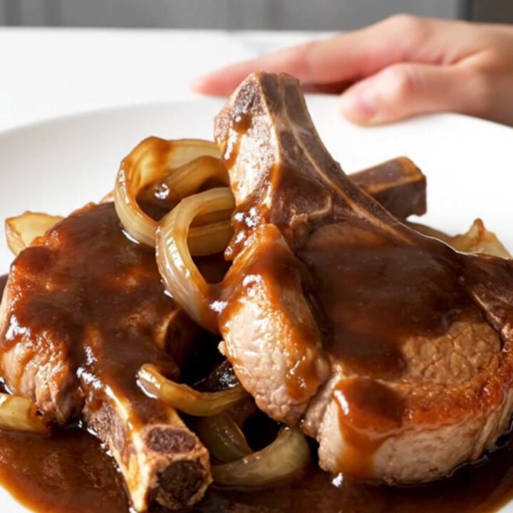 A close-up of tender, bone-in pork chops glazed in a dark, glossy root beer barbecue sauce with soft onions.