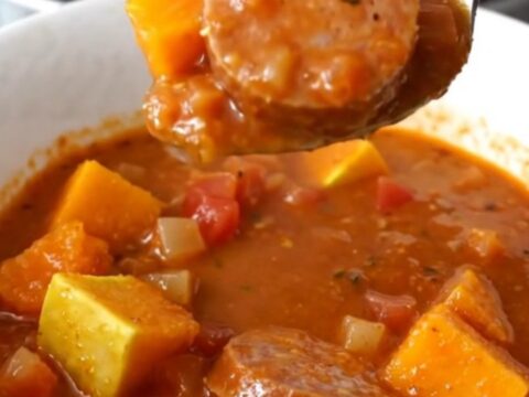 A close-up view of the slow cooker stew featuring sliced Italian sausage and tender butternut squash cubes in a rich tomato