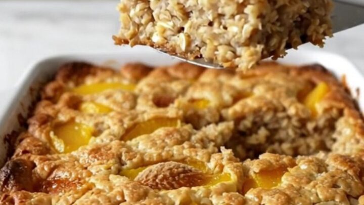 A top-down view of a rectangular baking dish filled with rolled oats, peach slices, and a golden brown sugar crust.