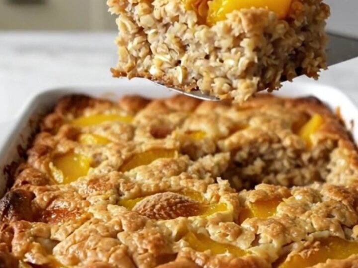 A top-down view of a rectangular baking dish filled with rolled oats, peach slices, and a golden brown sugar crust.