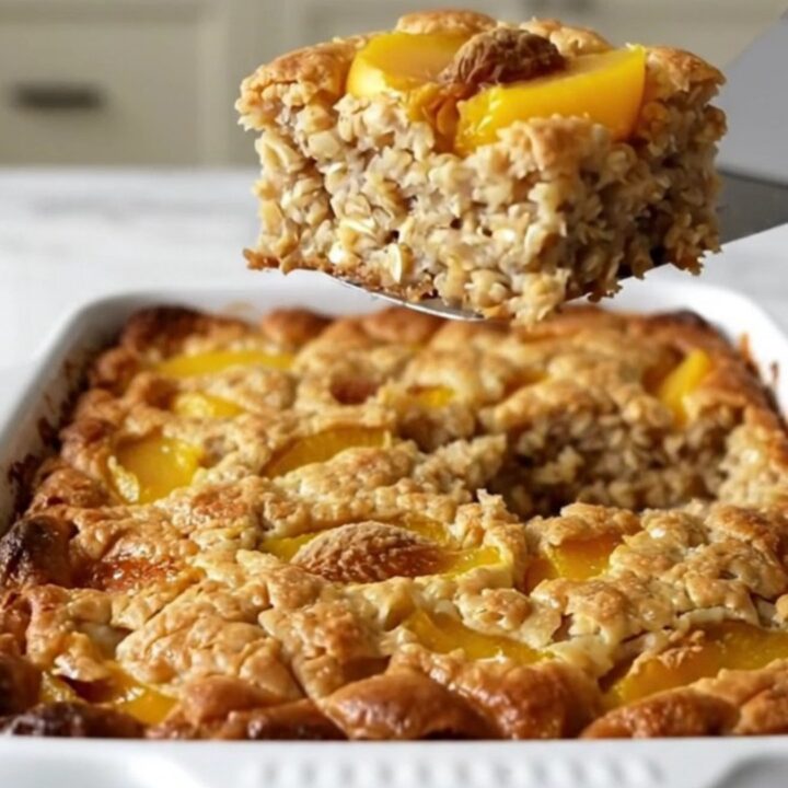 A top-down view of a rectangular baking dish filled with rolled oats, peach slices, and a golden brown sugar crust.