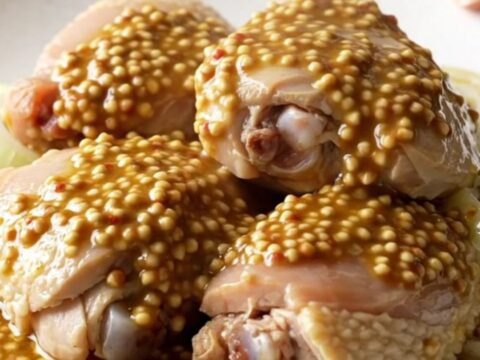 A close-up of tender, braised chicken thighs topped with soft, caramelized onion slices in a rich mustard sauce.