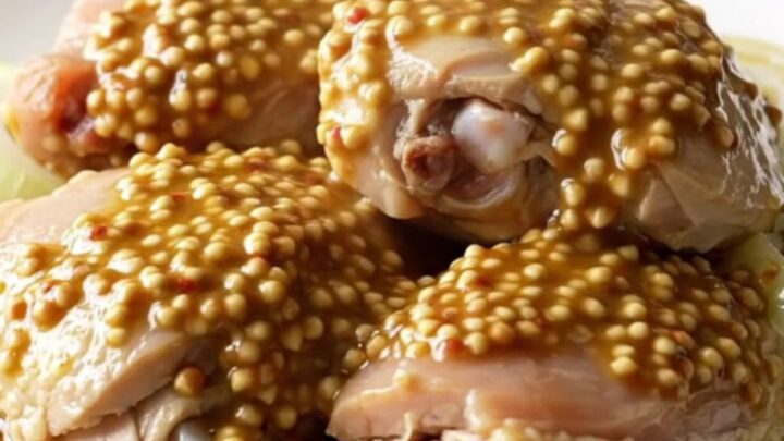 A close-up of tender, braised chicken thighs topped with soft, caramelized onion slices in a rich mustard sauce.