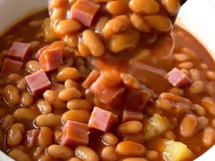 A top-down view of a slow cooker filled with diced ham, baked beans, pineapple chunks, and barbecue sauce ready to cook.