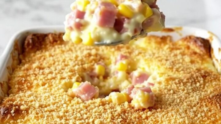 A top-down view of a rectangular ceramic baking dish filled with a creamy corn and ham casserole topped with golden cracker