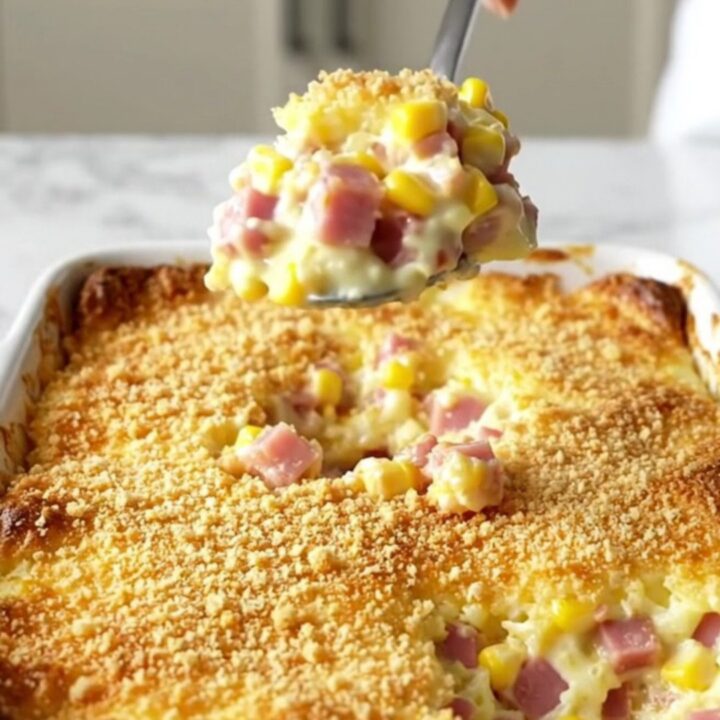 A top-down view of a rectangular ceramic baking dish filled with a creamy corn and ham casserole topped with golden cracker