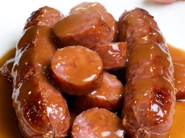 A close-up of slow-cooked kielbasa coins and baby carrots glazed in a glossy brown sugar sauce.