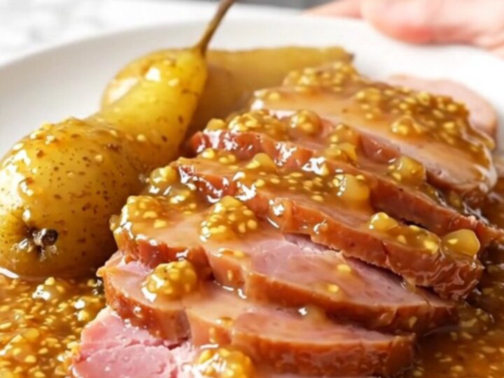 A platter featuring thick, succulent slices of slow-cooked ham arranged neatly next to tender, glazed pear halves.