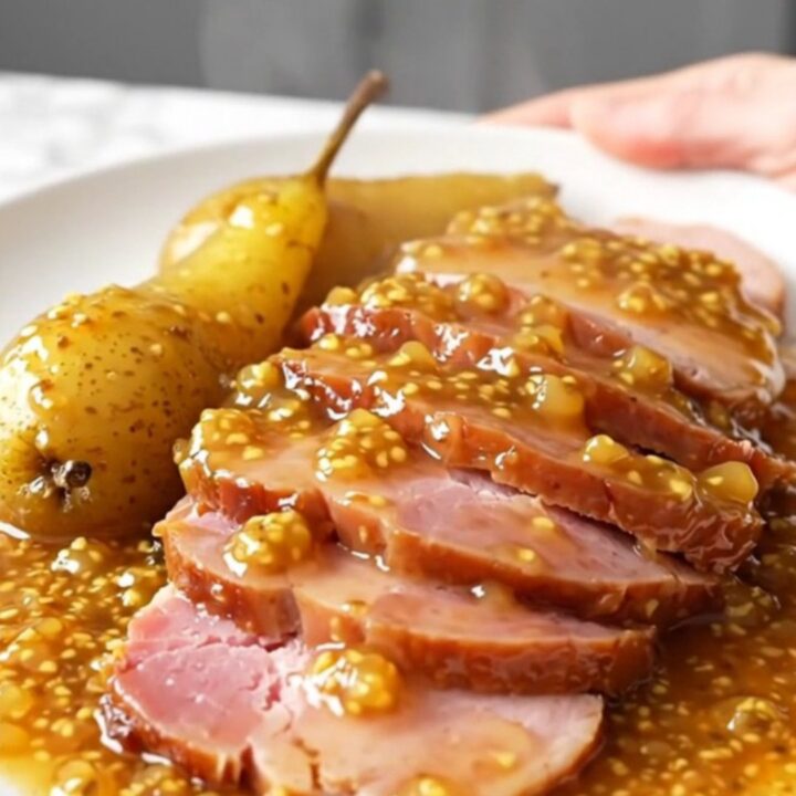 A platter featuring thick, succulent slices of slow-cooked ham arranged neatly next to tender, glazed pear halves.