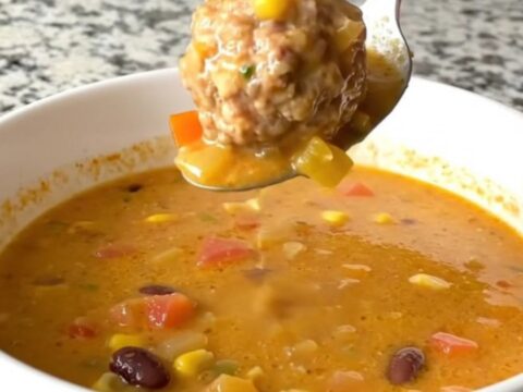 A steaming bowl of creamy taco meatball soup filled with meatballs, black beans, and corn.