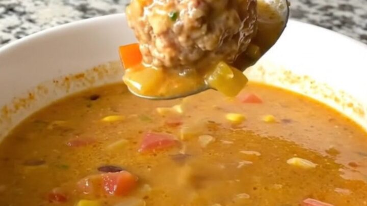 A steaming bowl of creamy taco meatball soup filled with meatballs, black beans, and corn.