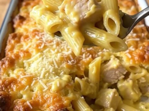 A large white enameled rectangular baker filled with a creamy lemon pepper chicken penne bake on a butcher-block counter.