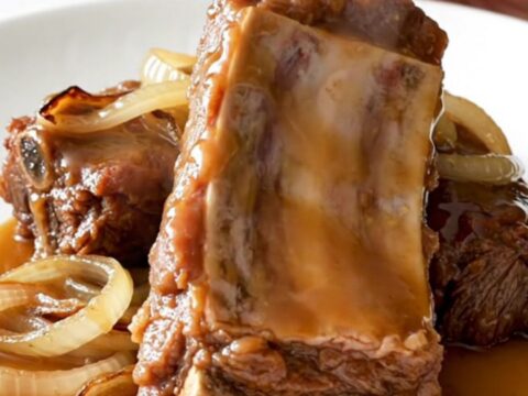A close-up of slow-cooked boneless beef ribs glistening with a maple Dijon glaze on a white plate.