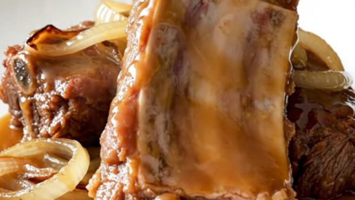 A close-up of slow-cooked boneless beef ribs glistening with a maple Dijon glaze on a white plate.