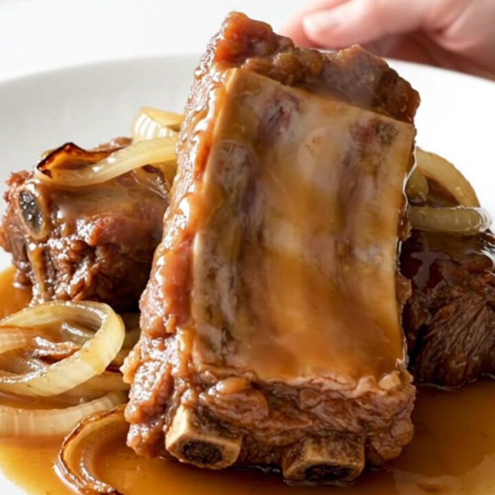 A close-up of slow-cooked boneless beef ribs glistening with a maple Dijon glaze on a white plate.