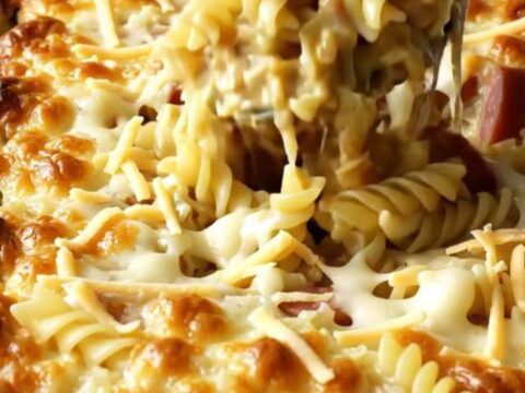 A golden, bubbling Polish Reuben Kielbasa Pasta Bake in a white ceramic dish on a beige countertop.