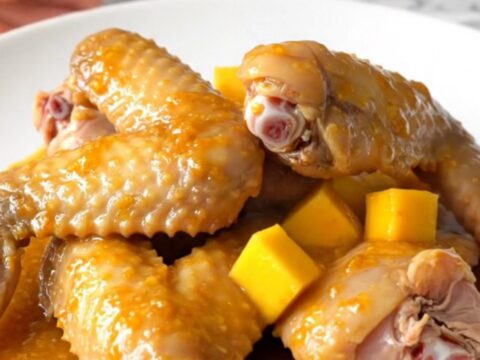 A close-up of slow-cooked turkey wings glazed in a bright orange mango habanero sauce on a white plate.