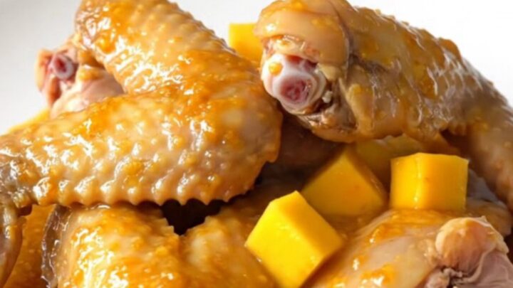 A close-up of slow-cooked turkey wings glazed in a bright orange mango habanero sauce on a white plate.