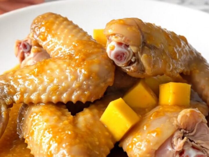 A close-up of slow-cooked turkey wings glazed in a bright orange mango habanero sauce on a white plate.