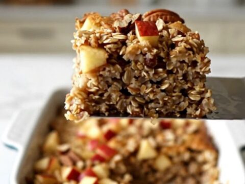 A top-down view of a rectangular ceramic dish filled with baked oatmeal, topped with diced red apples and pecans.