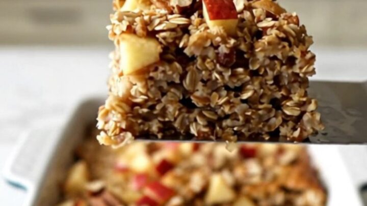 A top-down view of a rectangular ceramic dish filled with baked oatmeal, topped with diced red apples and pecans.