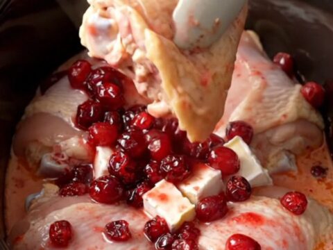 A close-up of tender chicken thighs covered in a creamy, pink cranberry and brie sauce inside a slow cooker.