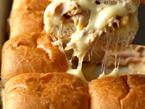 A rectangular baking dish filled with golden-brown Alabama white BBQ chicken sliders.