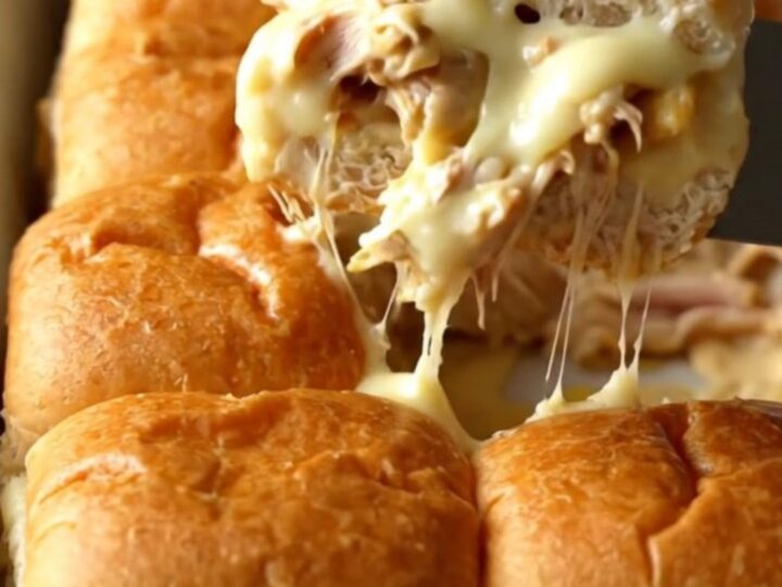 A rectangular baking dish filled with golden-brown Alabama white BBQ chicken sliders.
