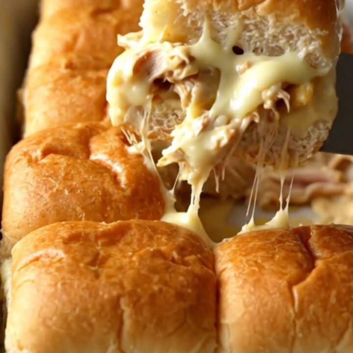 A rectangular baking dish filled with golden-brown Alabama white BBQ chicken sliders.