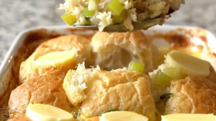 A golden-brown sweet roll stuffing bake in a white ceramic dish on a speckled granite surface.