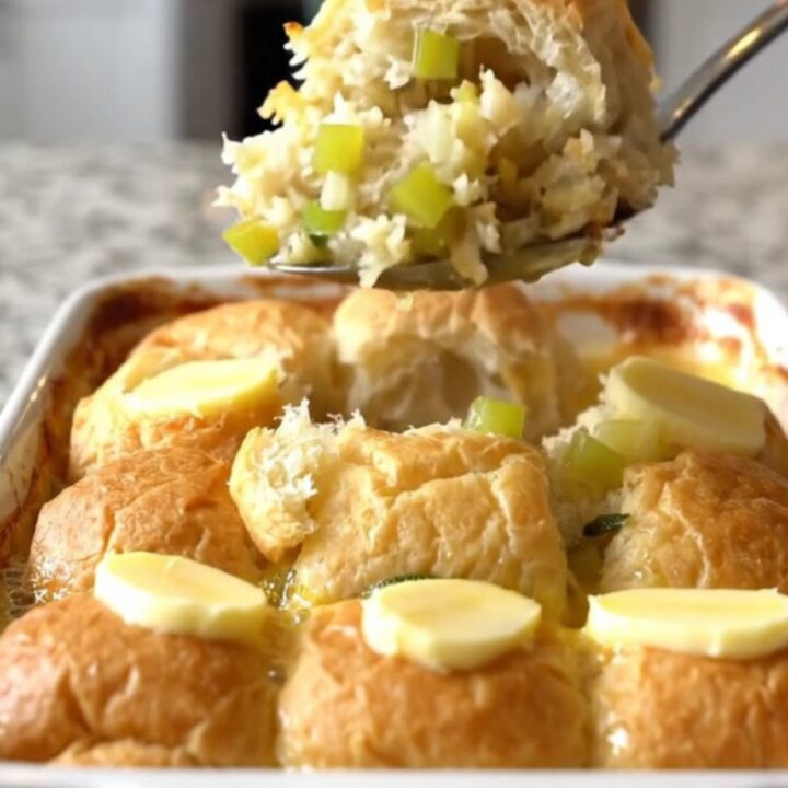 A golden-brown sweet roll stuffing bake in a white ceramic dish on a speckled granite surface.