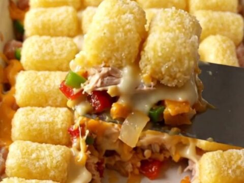A golden, bubbling Philly cheesesteak potato tot casserole in a white ceramic dish on a beige countertop.