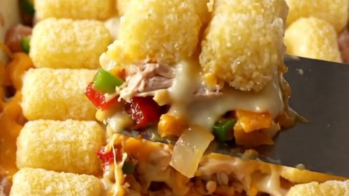 A golden, bubbling Philly cheesesteak potato tot casserole in a white ceramic dish on a beige countertop.