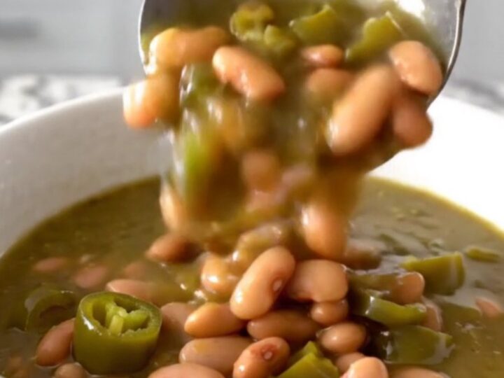 A close-up of a white bowl filled with a thick, green-hued pinto bean stew with steam rising gently.