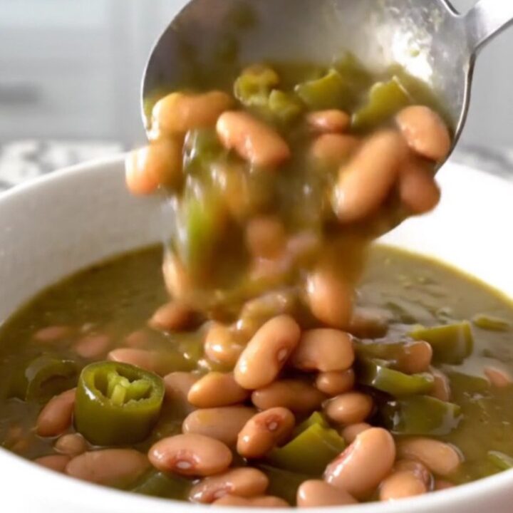 A close-up of a white bowl filled with a thick, green-hued pinto bean stew with steam rising gently.