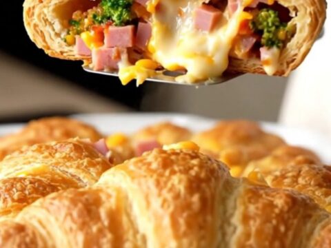 A golden, puffed ham and broccoli cheddar crescent bake in a white enameled dish.