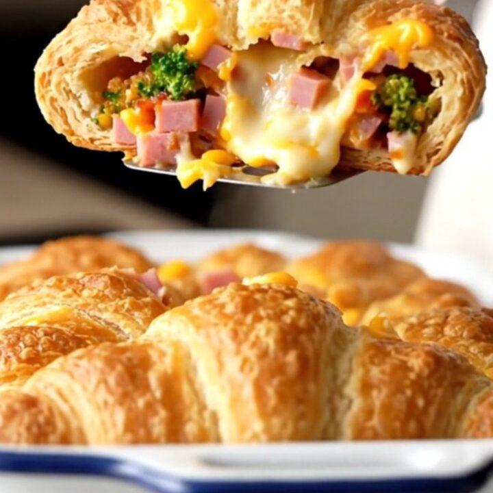 A golden, puffed ham and broccoli cheddar crescent bake in a white enameled dish.