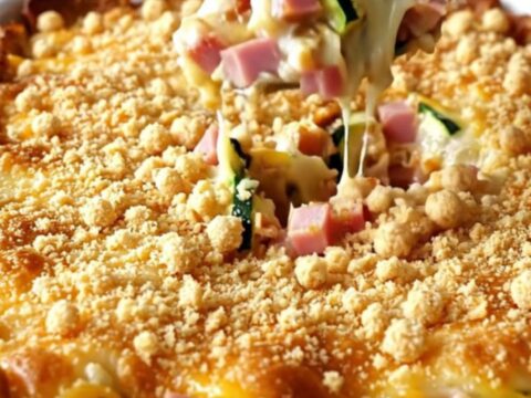 A creamy ham and Swiss zucchini casserole in a white baking dish with a golden cracker crumb topping.