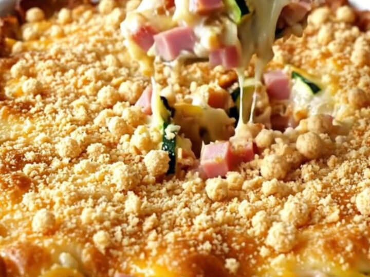 A creamy ham and Swiss zucchini casserole in a white baking dish with a golden cracker crumb topping.