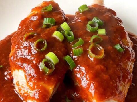A white oval slow cooker filled with raw turkey tenderloins, green onions, and a vibrant red gochujang sauce.